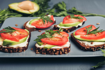 Healthy green veggie food concept. Yammy toast with cream cheese, avocado and juicy red tomato on grey table.