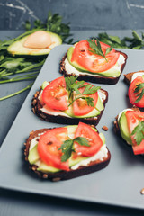 Healthy green veggie food concept. Yammy toast with cream cheese, avocado and juicy red tomato on grey table.