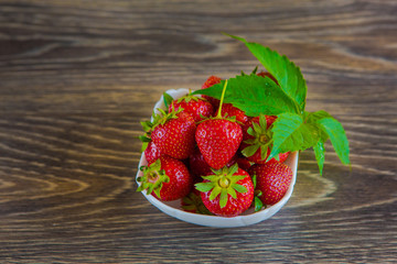 A small white porcelain bowl filled with juicy fresh ripe red strawberries. Textured table top. Fresh strawberries. Strawberries in a Bowl