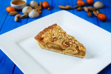 Homemade apple crumble pie sliced on square plate with kumquats and almonds on blue wooden background
