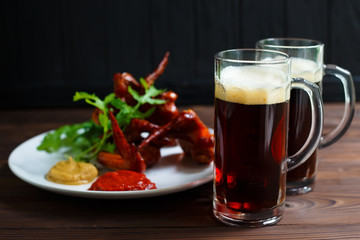 Two mugs of dark beer with delicious hot crusty grilled chicken wings with mustard and spicy tomato sauce