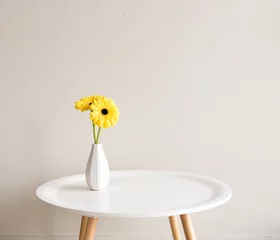 Papier Peint photo Gerbera Gerberas jaunes dans un petit vase blanc sur une table ronde sur fond neutre