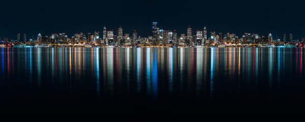 Fantastic nighttime panoramic city view with illuminated skyscrapers reflected on calm water. Ultra wide night time panoramic view of Seatle.