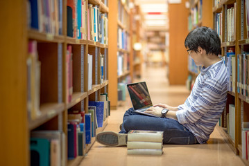 Young Asian man university student thinking about his project homework and using laptop computer in library, education research and self learning in university life concepts