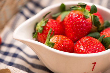 Bowl with fresh strawberry on blue wooden table.