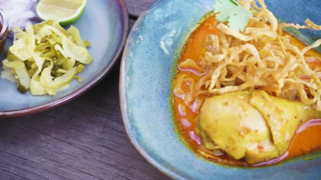 Chicken curried noodle soup (Khao soi kai) on the woodern table.