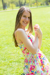 Obraz premium Portrait of young beautiful woman with long hair wearing flower dress in green spring park