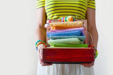 A woman holding a stack with colorful fabrics. Needle bed, scissors, measuring tape. Beige...
