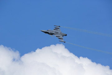 Modern jet fighter flying against a blue sky. White smoke trail.