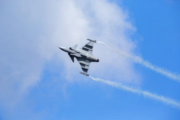 Modern jet fighter flying against a blue sky. White smoke trail.
