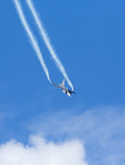 Modern jet fighter flying against a blue sky. White smoke trail.
