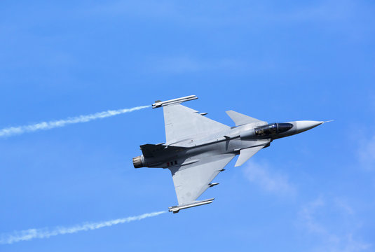Fototapeta Modern jet fighter flying against a blue sky. White smoke trail.