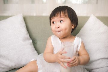Obraz na płótnie Canvas Cute baby girl drinking milk with milk mustache at home