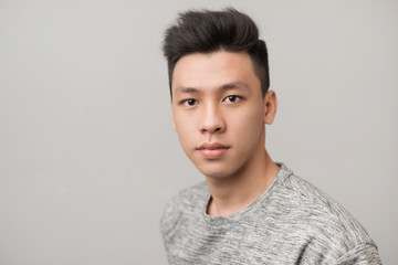 Portrait of good looking asian man over gray background.