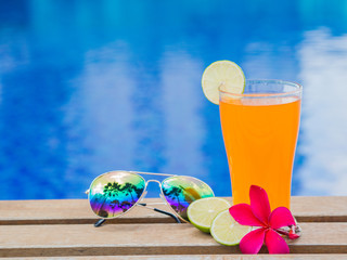 Red frangipani (plumeria) flowers, Orange juice and a piece of lemon at the side of swimming pool. Vacation, beach, summer travel concept