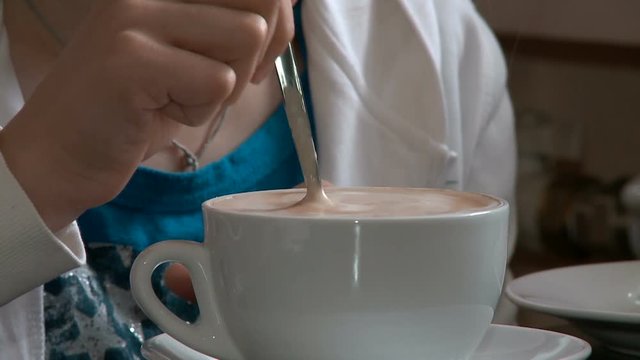 Close-up of a young girl's hand stirring with a spoon of foam in a cup with cappuccino