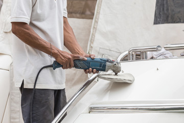 Yacht maintenance. A man polishing side of the white boat in the marina