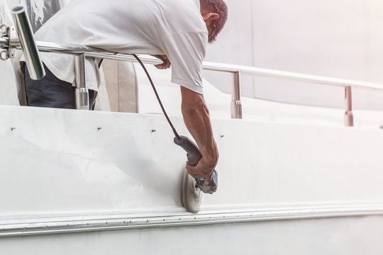 Yacht maintenance. A man polishing side of the white boat in the marina