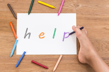 "HELP" in white paper writing by right foot of disabled people on wooden desk. Use for donation for disabled concept. Focus on foot top view