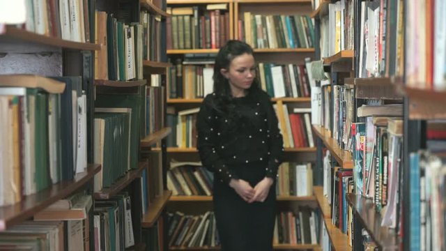 Beautiful young woman picking out textbook at library of university