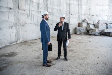 Two professional mature architects with blueprint working at construction site