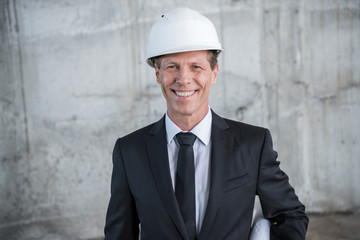 Professional middle aged architect in helmet smiling at camera