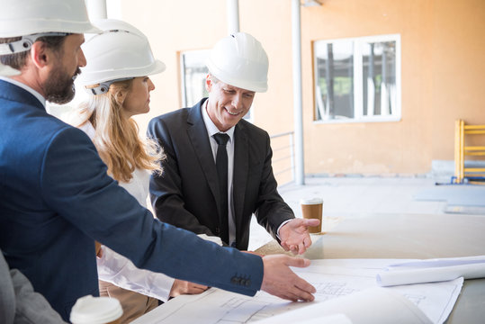 mature contractors in formal wear working with blueprints at construction
