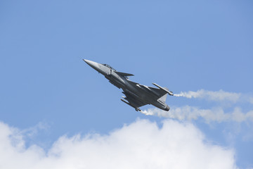 Fototapeta na wymiar Modern tactical jet fighter is flying slowly with white smoke trail. Blue sky with clouds in the background.