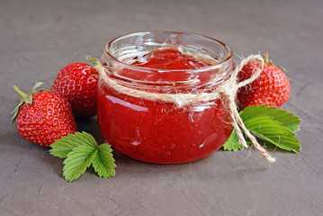 Ingredient for healthy breakfast. Homemade jam in open glass jar with fresh strawberry