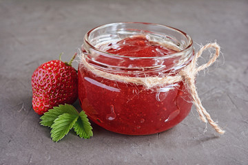 Ingredient for healthy breakfast. Homemade jam in open glass jar with fresh strawberry