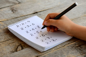 Child solves mathematics examples. Child holds a black marker in his hand. Notebook sheet with multiplication table examples. Studying a multiplication table concept © onlynuta