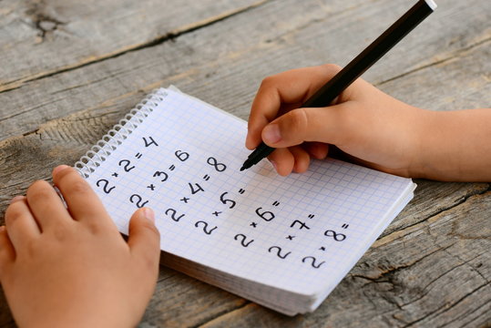 Student solves multiplication examples. Child holds a black marker in his hand and writes answers. Notebook with multiplication table examples. Teaching a multiplication table concept