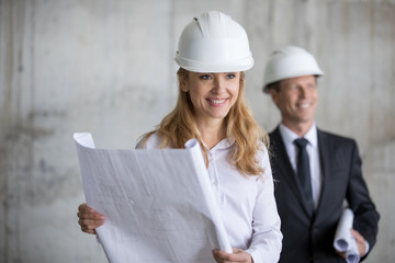 Smiling middle aged businesswoman holding blueprint while smiling colleague standing behind