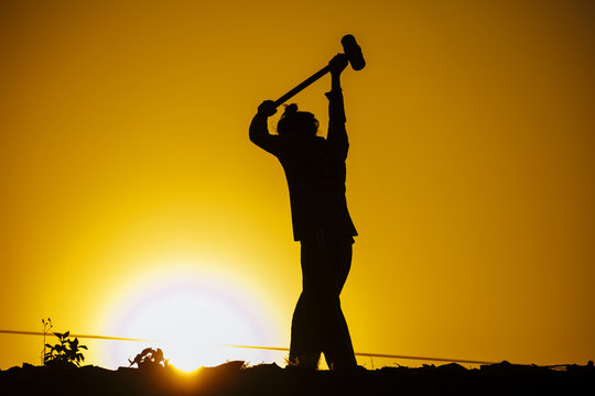 Action silhouette labor man hitting his hammer over sunset. Image made warm tone.