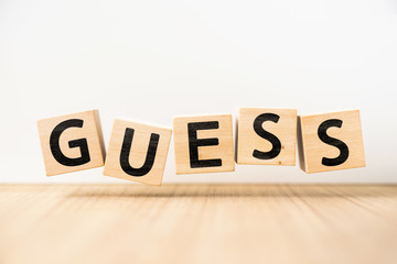 Surreal abstract geometric floating wooden cube with word "GUESS" concept float on wood floor white background.