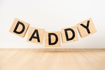 Surreal abstract geometric floating wooden cube with word "DADDY" concept float on wood floor white background.