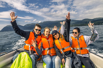 Portrait of young and attractive people, friends in the motorboat driving somewhere on a picnic. Happy faces, having fun, Norway. Raised up hands. - obrazy, fototapety, plakaty