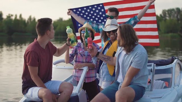 Slow motion of diverse group of cheerful friends having drinks on pier near boat celebrating Independence day and make selfie with smartphone mounted on monopod