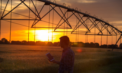 Farmer holding tablet in field at sunset