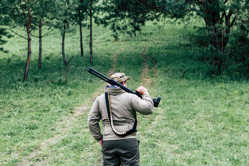 Fototapeta premium Hunter with a gun. Standing in the forest and waiting for prey
