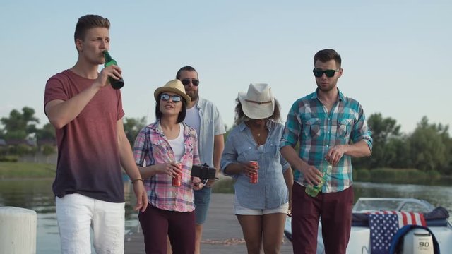 Young happy multiethnic people walking with drinks in pier and having fun and make selfie