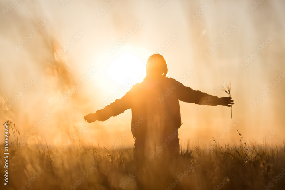 Wall mural Middle aged caucasian woman standing in the sunlit field with open arms, embracing nature