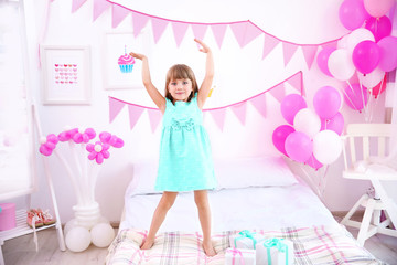 Cute girl standing on bed at home decorated for birthday party