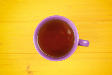 Lilac cup with tea on yellow background