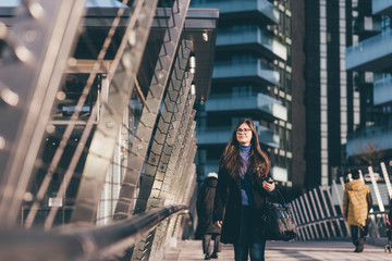 Young business woman outdoor walking in the city holding smart phone smiling - business, shopping,...