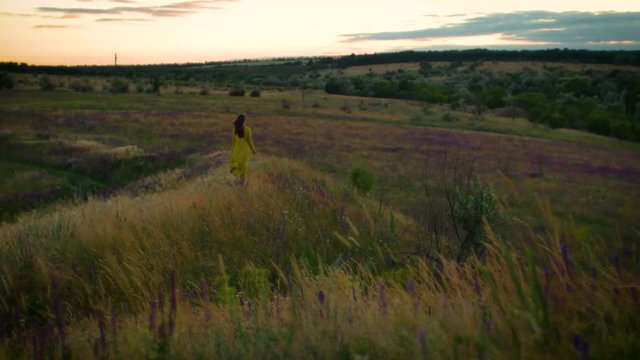 young woman walking on winded flowers field in sunset time