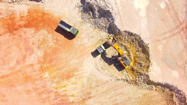 Aerial view of a excavator loading a truck in open cast mine or on construction site. Heavy industry from above. Industrial background from drone. 