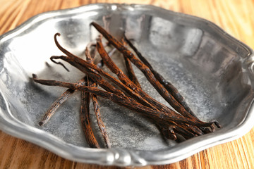 Fototapeta premium Metal plate with dried vanilla sticks on wooden table, closeup