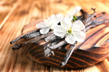 Board with dried vanilla sticks and flowers on wooden table, closeup