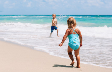 little girl and boy run play with waves on beach